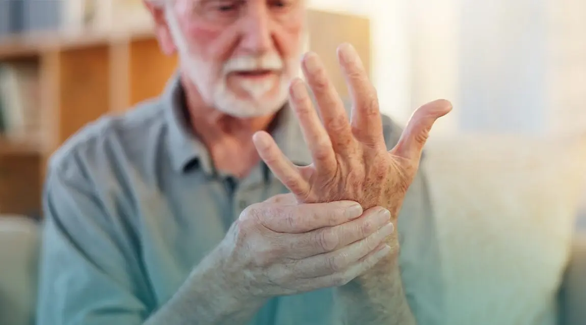 Adulto mayor revisando su mano por dolor por artritis.