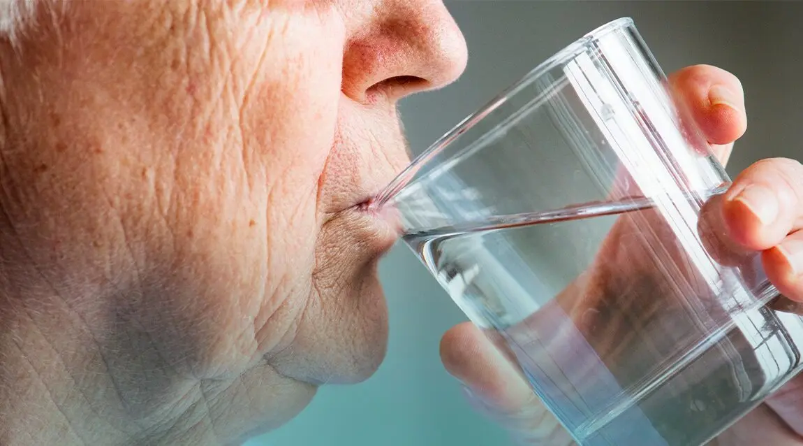 Adulto mayor cuida su hidratación con un vaso de agua.