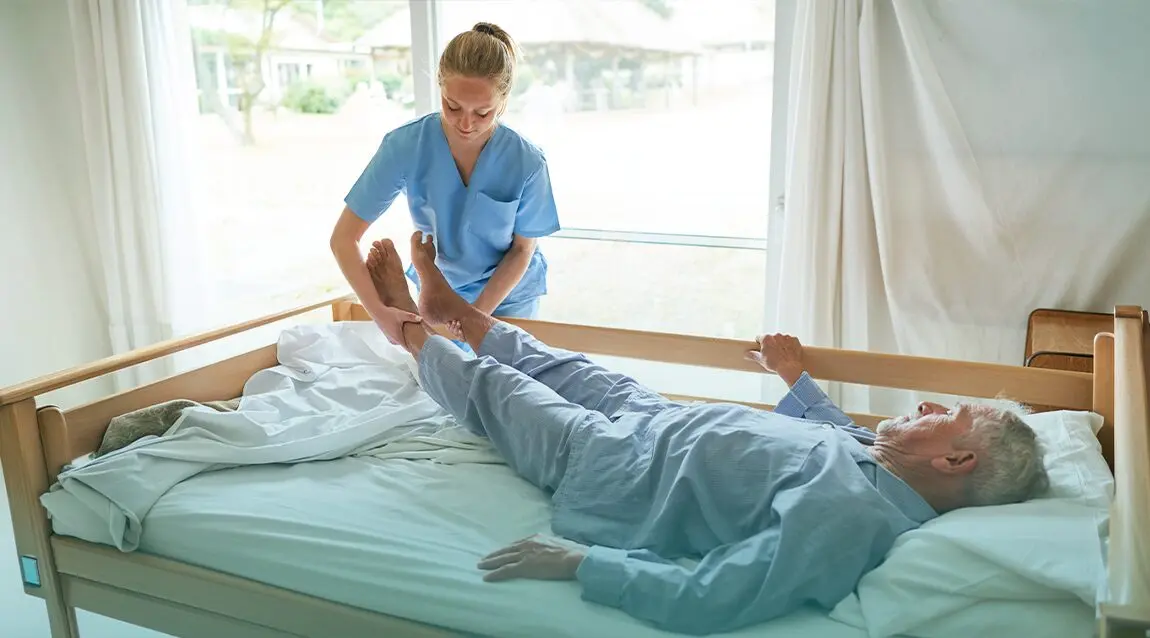 Adulto mayor siendo asistido para cambiar de posición en la cama y prevenir las ulceras por presion